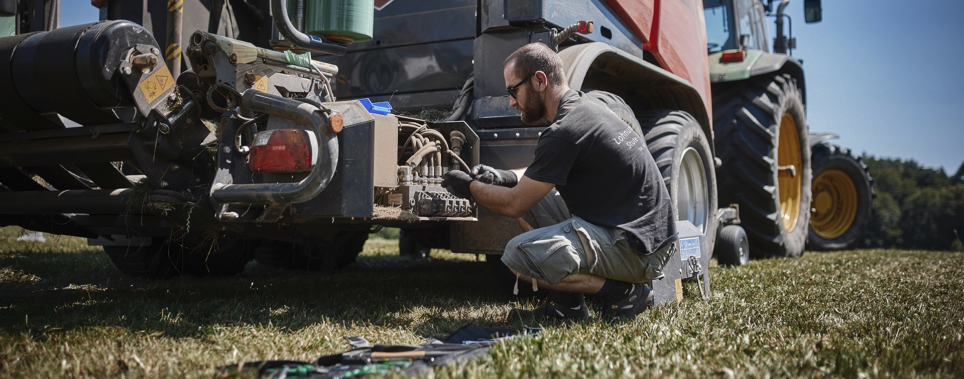 Mann auf Feld repariert Ballenpresse mit Schraubenschlüssel